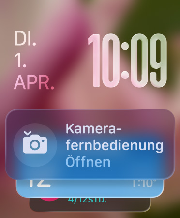 Das Widget für die Kamerafernbedienung erscheint unten auf dem Bildschirm, oben rechts sind transluzente Zeitziffern zu sehen, das Datum befindet sich oben links