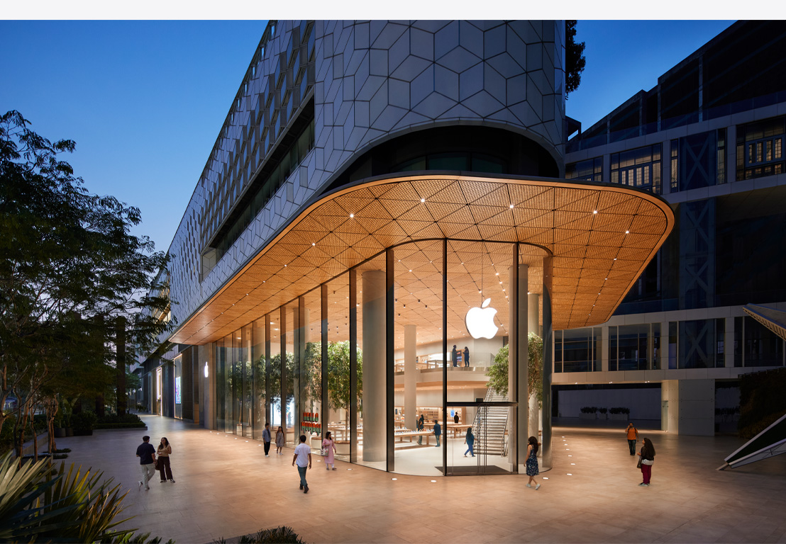 Apple Store de nuit, baies vitrées, lumière allumée à l’intérieur, logo Apple centré au-dessus de la porte d’entrée.